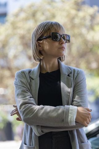 Confident urban professional wearing sunglasses and gray blazer, crossing arms in city