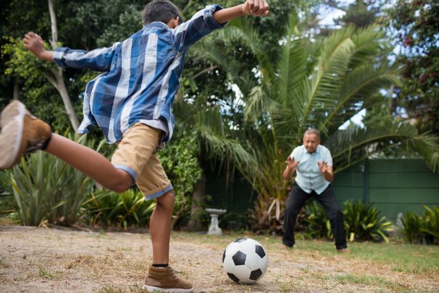 Boy playing soccer with grandfather on field in yard