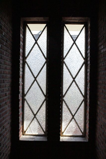 Lattice windows with textured glass allowing sunlight into a room with brick walls. Suitable for use in design and architecture projects, home decor inspiration, or illustrating concepts of vintage and traditional interior designs.