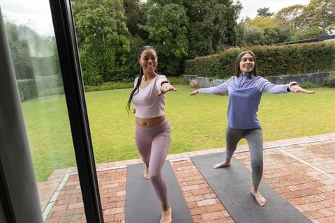 Outdoor yoga duo practicing warrior pose on brick patio in colorful activewear