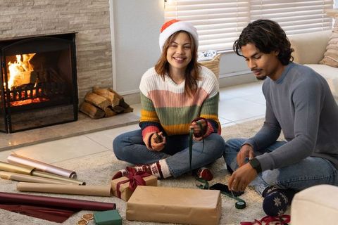 Couple wrapping christmas gifts by fireplace, woman wearing santa hat, cozy holiday moment