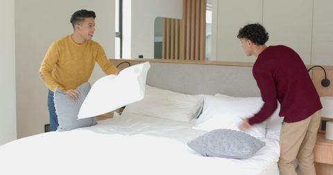 Happy friends enjoying pillow fight in modern bedroom