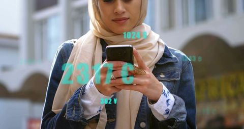 Woman wearing beige hijab checking smartphone with augmented currency overlays in city