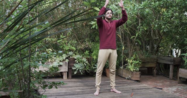 Man standing in green garden performing yoga pose. Useful for topics on outdoor activities, mental health, mindfulness, wellness, and fitness.