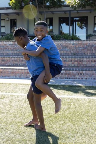 African american boys playing piggyback on school turf smiling in sunlight