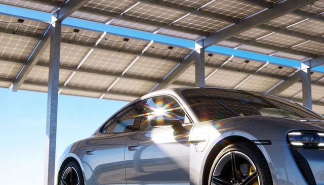 Silver electric sedan charging under solar canopy with sun flare reflections