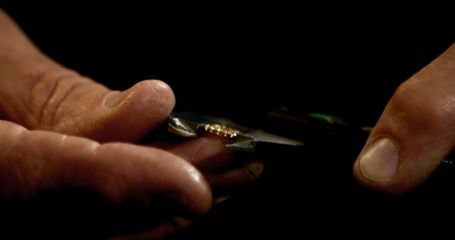 Depicts craftsman's hands working on a small jewelry piece using fine tools. Ideal for content related to jewelry making, craftsmanship tutorials, artisanal skills, or precision handiwork displays.