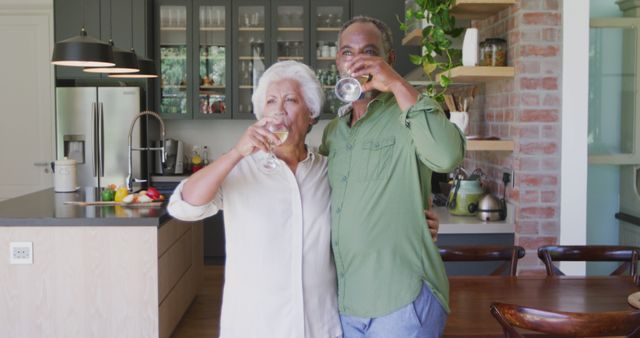 Happy senior biracial couple drinking wine together in sunny kitchen. Senior lifestyle, togetherness, relaxation and domestic life.