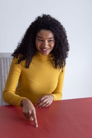 Woman in Yellow Turtleneck Pointing at Red Table in Studio