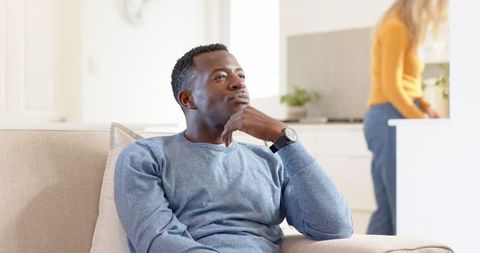 Pensive man relaxing at home while partner in kitchen