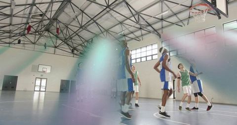 Male basketball players contesting rebound under hoop in gymnasium during practice drills