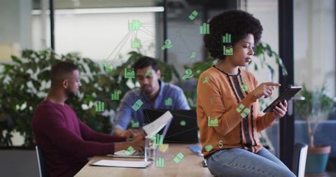 Woman tapping tablet while team collaborates in modern office with green analytics overlay
