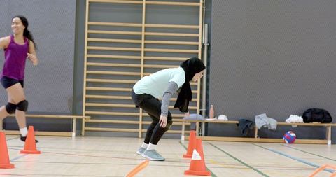Muslim athlete practicing cone agility drill with diverse female teammates on gym court