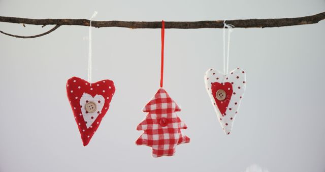 Three handmade Christmas ornaments in the shape of a heart and a tree hang from a branch against a plain background, with copy space. These festive decorations evoke a sense of holiday warmth and handmade craft charm.