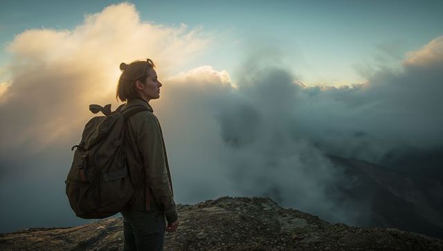 Solo hiker standing on mountain ridge gazing over misty cloud sea at sunrise with backpack