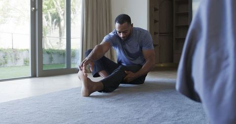 Man stretching hamstring on rug at home during morning fitness routine with natural light