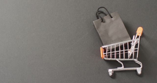 Miniature shopping cart containing black shopping bags placed on a grey surface. This visual represents themes such as modern shopping, e-commerce, and retail. Suitable for online business promotions, marketing materials, and advertisements related to shopping and consumerism.