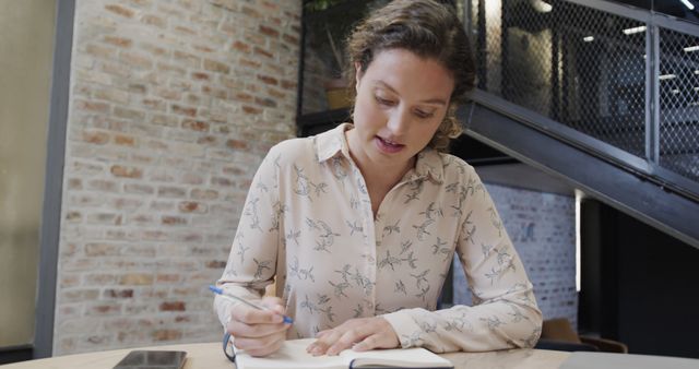 Young woman writing in notebook at modern loft office - Download Free Stock Images Pikwizard.com