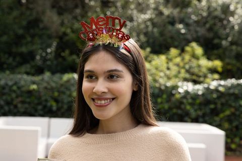 Smiling woman wearing merry christmas headband and beige sweater in backyard garden