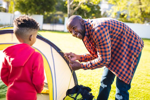 Happy african american father and son pitching tent in their backyard. Spending quality time at home, domestic life and family concept.