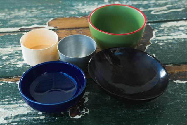 This image shows a variety of empty bowls placed on a rustic wooden table. The bowls are of different materials and colors, including ceramic, metal, and wood. This image can be used for themes related to kitchenware, dining, home decor, and rustic settings.