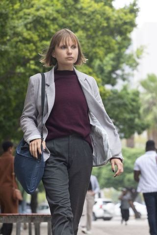 Young professional walking tree-lined urban sidewalk wearing blazer and carrying navy tote