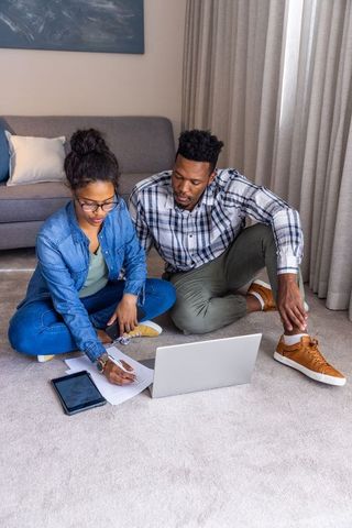 Couple working together on home finances using laptop and tablet, planning budget and documents