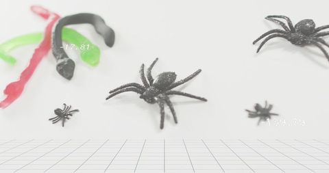 Sparkling black spider sitting on white table with gummy worms, grid and numeric overlay