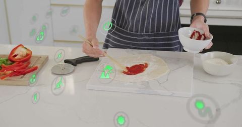 Teen spreading sauce on pizza dough in modern kitchen