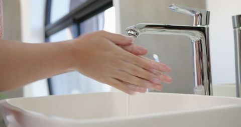 Washing Hands Under Running Water in Modern Bathroom