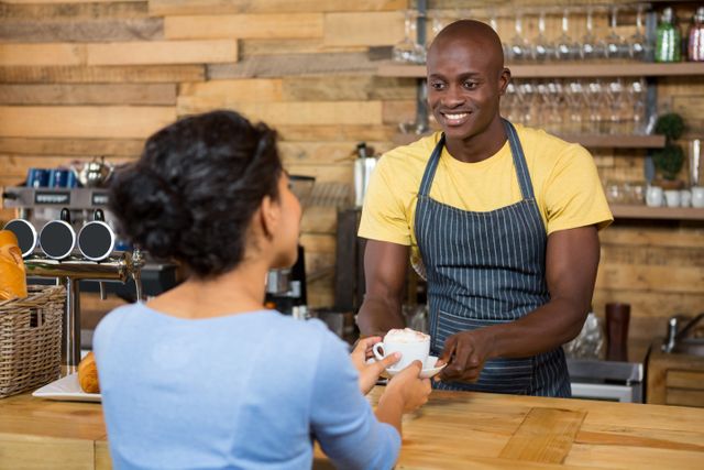 Barista in a cozy cafe serving a cup of coffee to a customer. Ideal for use in articles or advertisements related to coffee shops, customer service, hospitality industry, small businesses, and friendly service environments.
