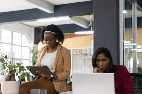 Female Colleagues Collaborating with Tablet and Laptop in Daylit Modern Office