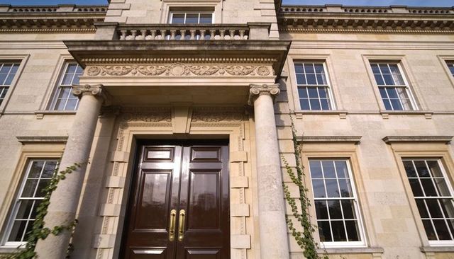 Neoclassical manor entrance featuring glossy double doors, fluted columns and climbing ivy