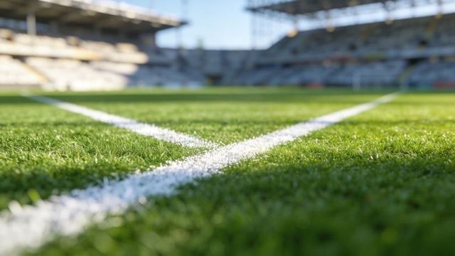 Close-up football pitch corner line on lush green turf with stadium stands and sunlit shadows