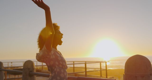 Woman with arms raised, feeling joyful and free, celebrating at ocean during sunset. Ideal for content related to happiness, freedom, summer getaways, travel experiences, motivational themes, and rejuvenation.