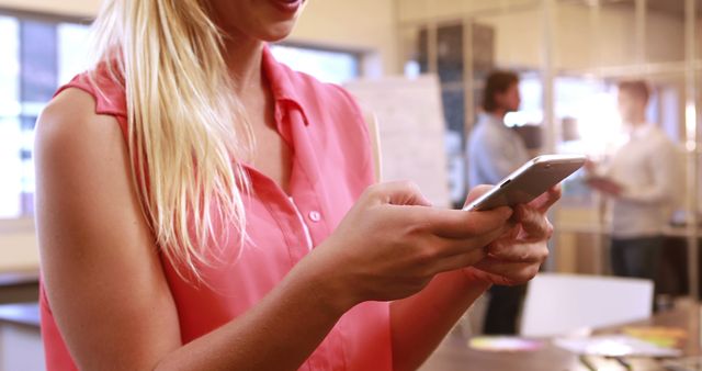 Young woman working or communicating on her smartphone in an office environment. Suitable for business, technology, communication, and modern workplace themes. Perfect for articles, blogs, advertisements, and social media posts highlighting professional women, mobile technology, or digital communication.