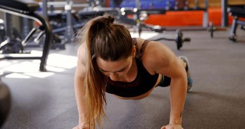 Fit woman performing push-up on rubber gym flooring wearing dark sports bra and shorts