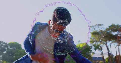 Leaning black man wearing sunglasses and blue jacket with digital wireframe halo overlay sunlit park