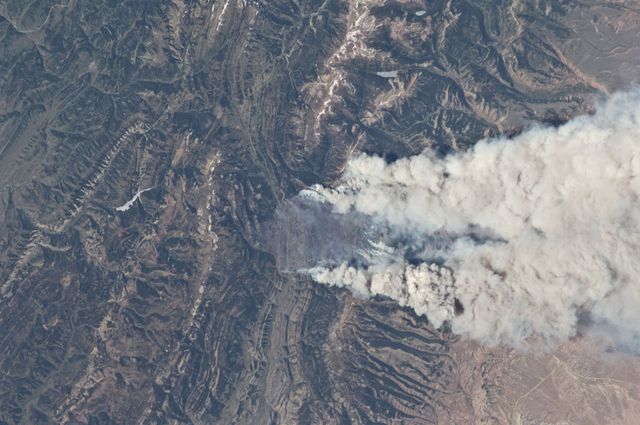 Aerial view shows Fontenelle fire spreading in Wyoming, 18 miles west of Big Piney, as seen from the International Space Station on June 27, 2012. Thick plumes of smoke are clearly visible, showing the fire's extensive impact. This image can be used in news articles about wildfires, environmental studies, or space perspectives. It highlights the severity of natural disasters and offers insight into the extent of fire damage. Suitable for environmental reports, educational materials, and articles on climate change.