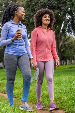 African american friends walking in park wearing activewear, holding reusable water bottles