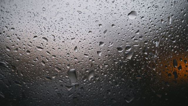 Rain-dappled windowpane showing condensation droplets and moody city bokeh lighting