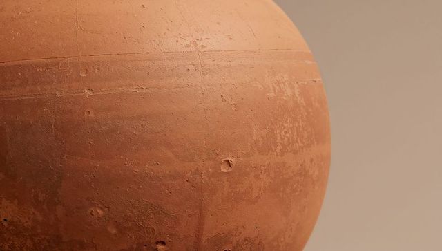 Terracotta sphere sculpture showing weathered pitted texture on neutral beige backdrop