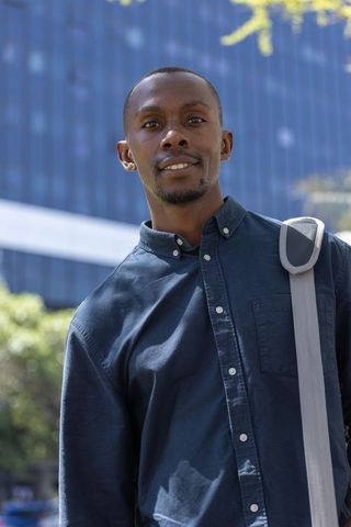 Confident young african man standing in front of glass office tower carrying shoulder bag