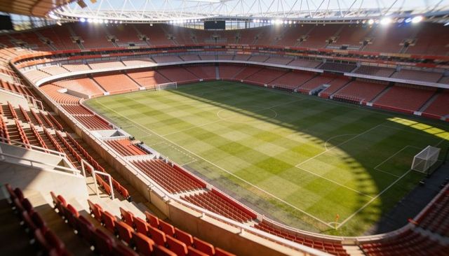 Sunlight casting curved shadow across empty football pitch with goals and striped turf