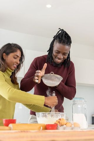 Young couple baking together in modern kitchen sifting flour and whisking batter