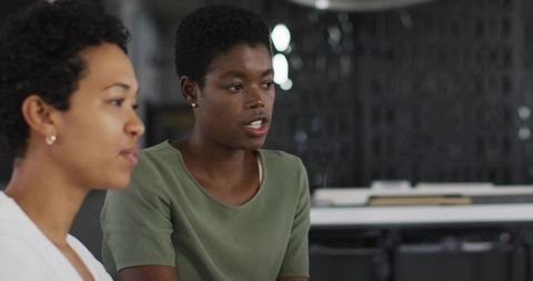 Two Professional Women Collaborating in Modern Office During Team Discussion Over Papers