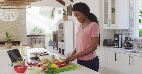 Chopping fresh vegetables on marble kitchen island with tablet recipe in bright modern kitchen