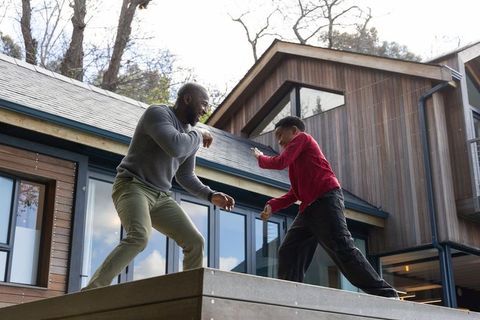 African american father sparring with teen son on modern deck, playful family bonding