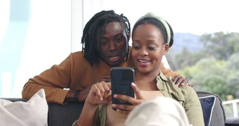 African American Couple Sharing Joyful Smartphone Moment on Couch in Bright Living Room
