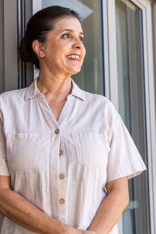 Mature woman standing by sliding glass door gazing outward with serene, hopeful expression